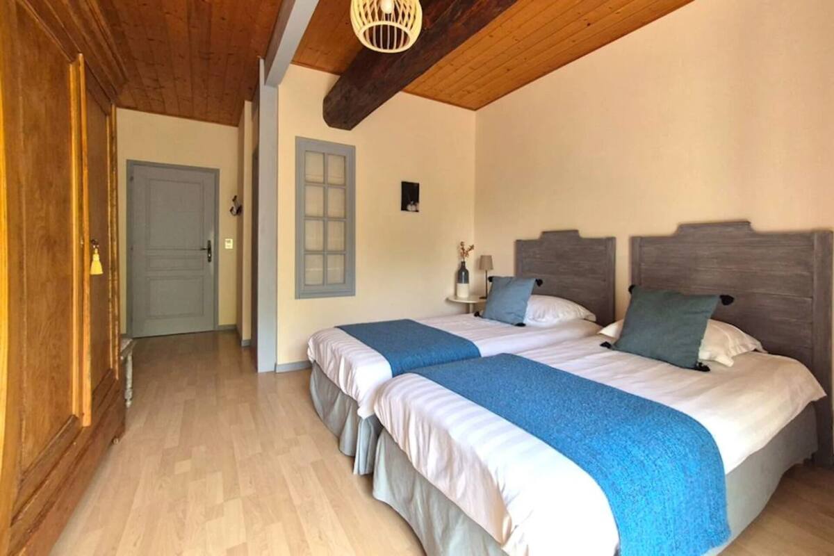 Ein Schlafzimmer mit zwei Betten, Holzboden, Holzbalkendecke und einem kleinen Nachttisch mit Lampe.