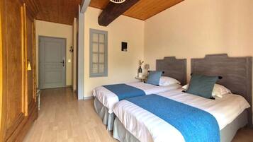 A bedroom with two beds, wooden flooring, a wooden ceiling, and a small bedside table with a lamp.