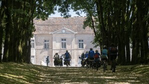 A group of cyclists on a paved path leading to a historic building with a symmetrical facade and a central entrance. - Le Tilleul de Ray (Ray-sur-Saone)