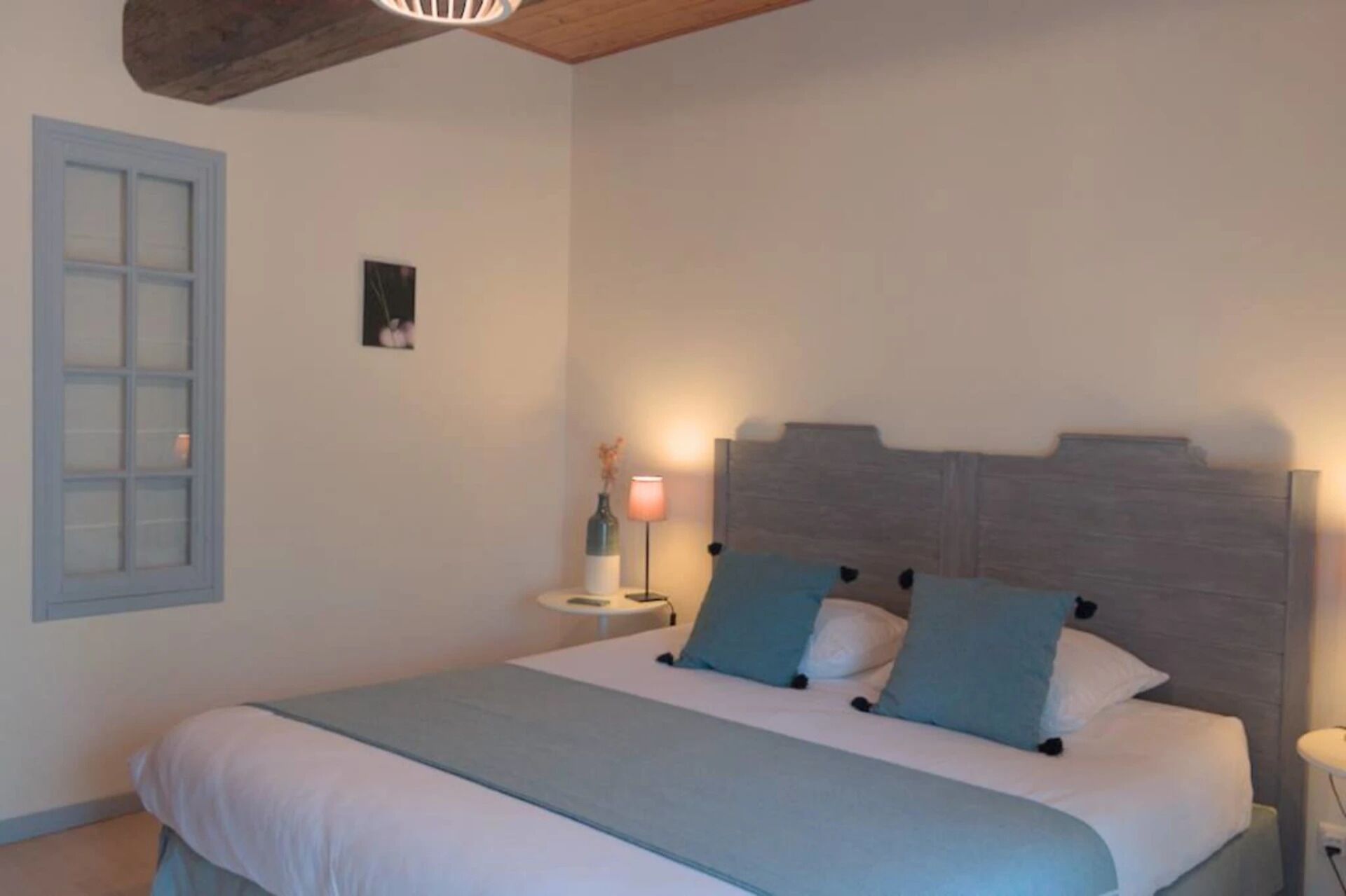 Une chambre à coucher avec un lit, une table de chevet, une lampe et une fenêtre donnant sur l’extérieur.