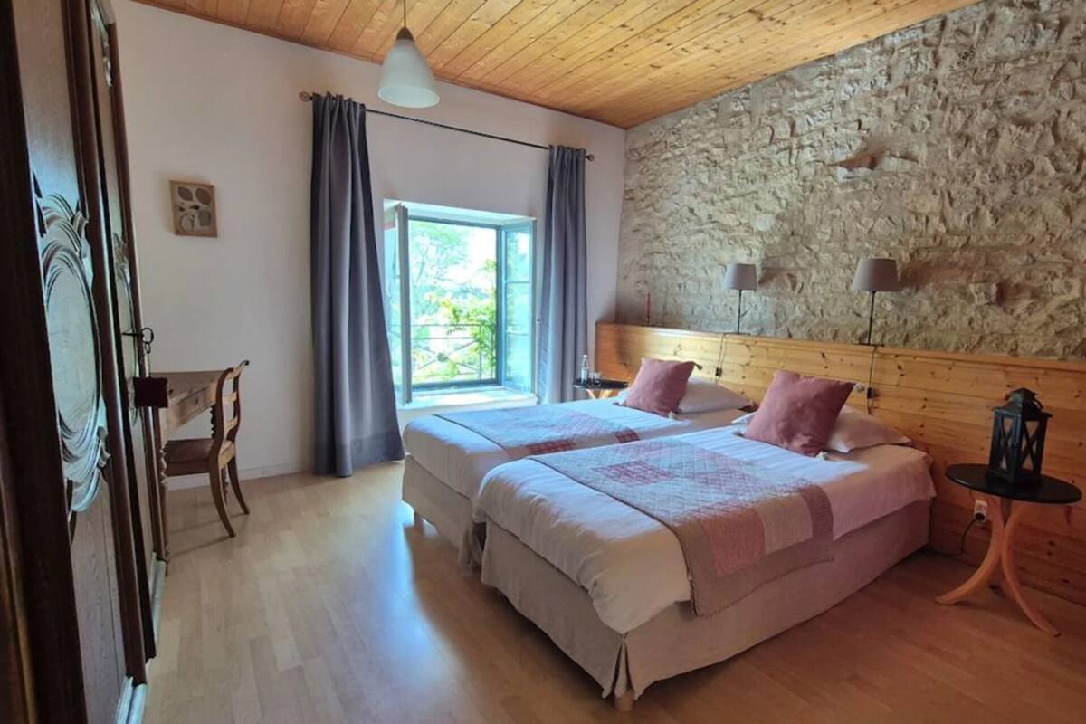Ein Schlafzimmer mit zwei Betten, einer Steinwand, einer Holzbalkendecke und einem Fenster mit Vorhängen.