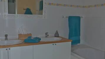 Een badkamer met twee wasbakken, een spiegel, een handdoekhouder en een bad.