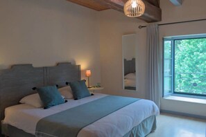 A bedroom with a large bed, a bedside table with a lamp, a window with a view of greenery, and a mirror on the wall. - Le Tilleul de Ray (Ray-sur-Saone)