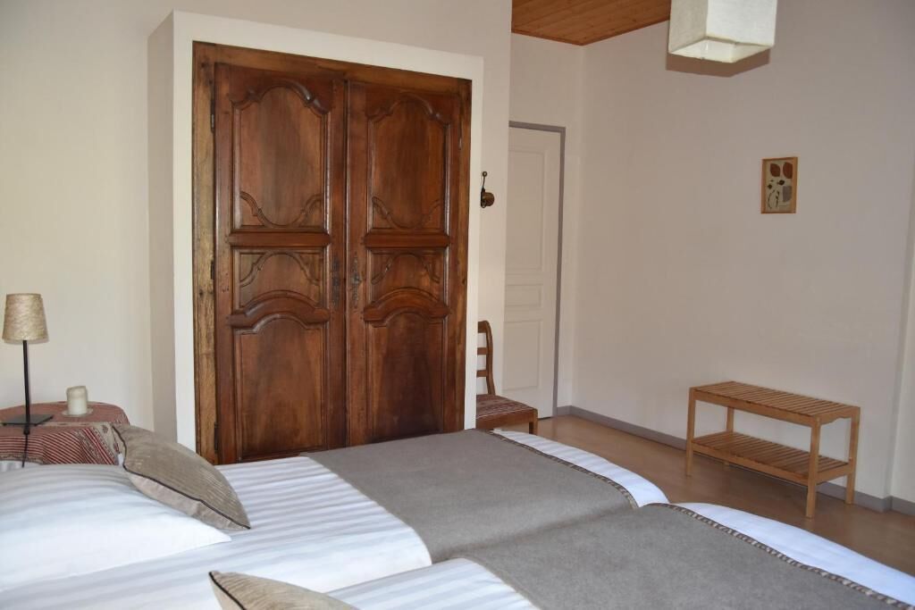 Un dormitorio con un gran armario de madera, una cama con ropa de cama a rayas, una pequeña mesa de madera y una silla.