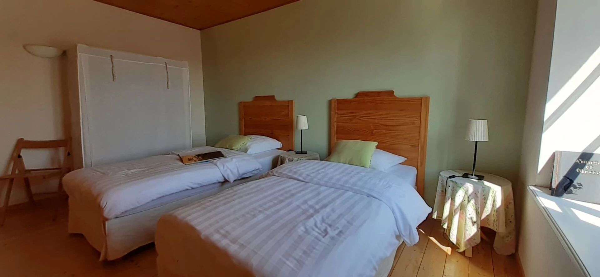 Una habitación con dos camas, una silla, una mesita con lámpara y una ventana con cortinas.