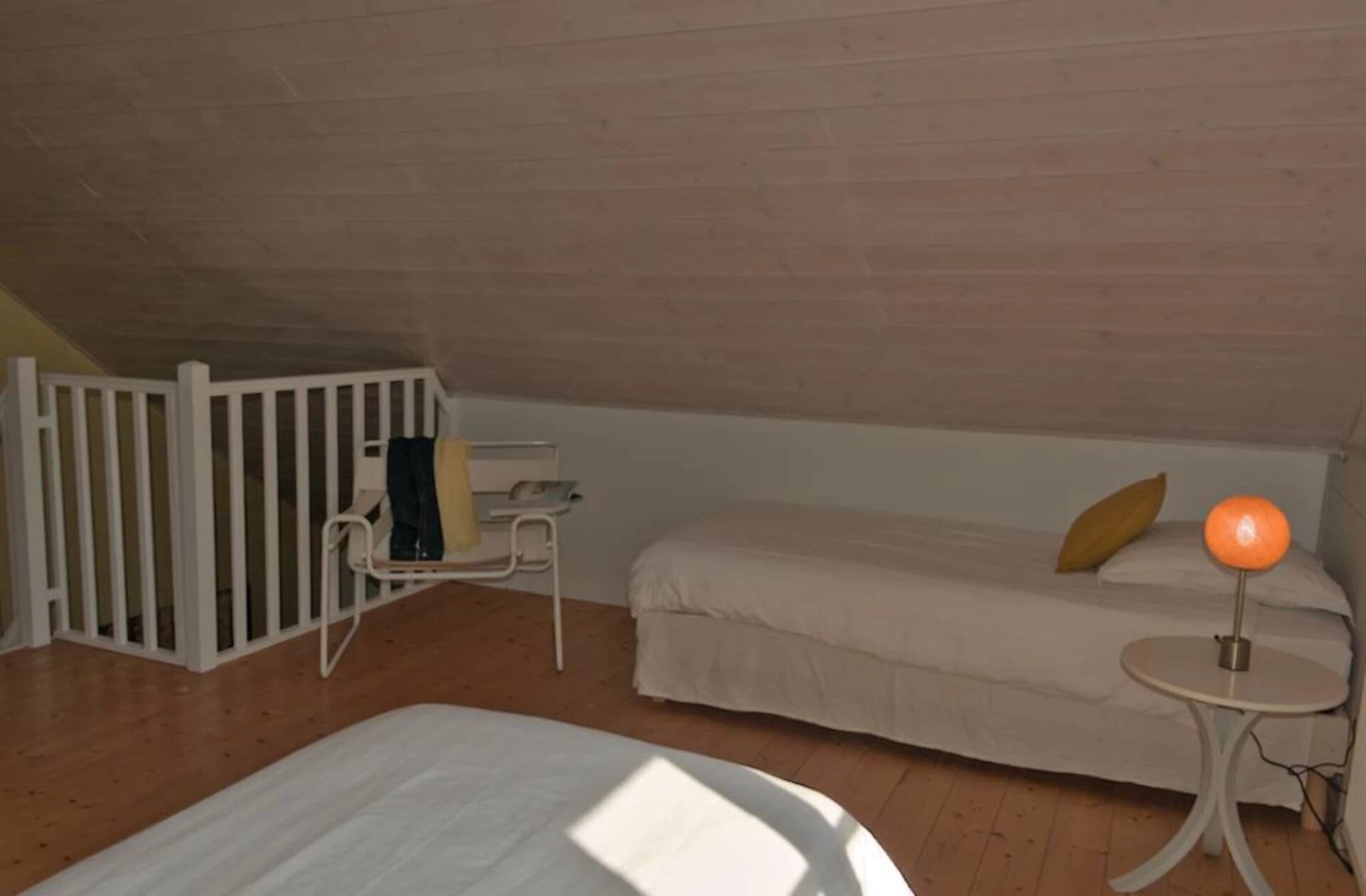 Una habitación con literas, una pequeña mesa blanca con lámpara y una silla blanca.