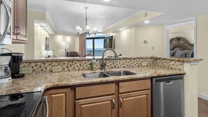 A modern kitchen with a granite countertop, stainless steel sink, and wooden cabinets. - Sand Dunes Resort Unit 1406 - Ocean View! (Myrtle Beach)