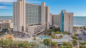 A hotel with multiple buildings, a parking area, and a pool with palm trees. - Sand Dunes Resort Unit 1406 - Ocean View! (Myrtle Beach)
