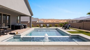 A modern outdoor pool area with a hot tub, seating, and a view of the desert landscape.