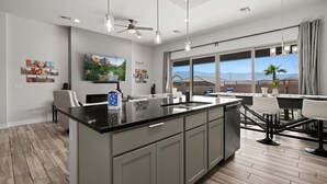 A modern kitchen with a large island, a dining area with a view, and a ceiling fan.