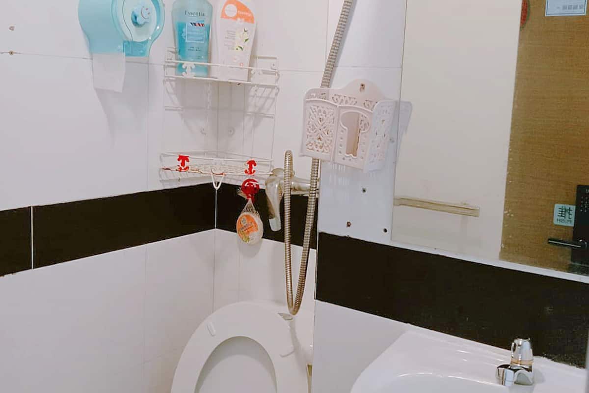 A bathroom with a toilet, a sink, and a shower. There are toiletries on a shelf and a mirror on the wall.