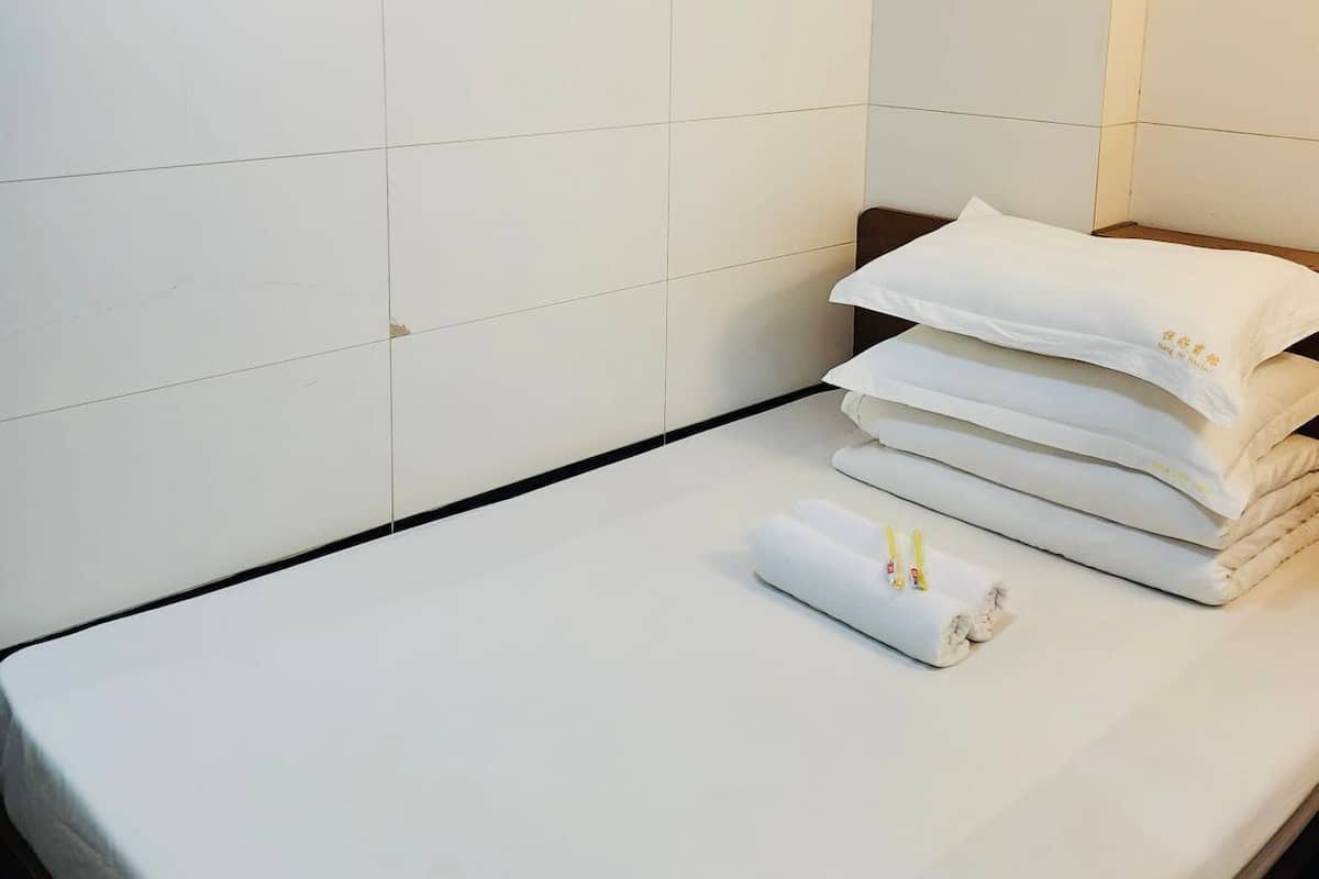 A neatly made bed with white linens and a rolled towel, a black edge along the bed's side, and a white tiled wall.