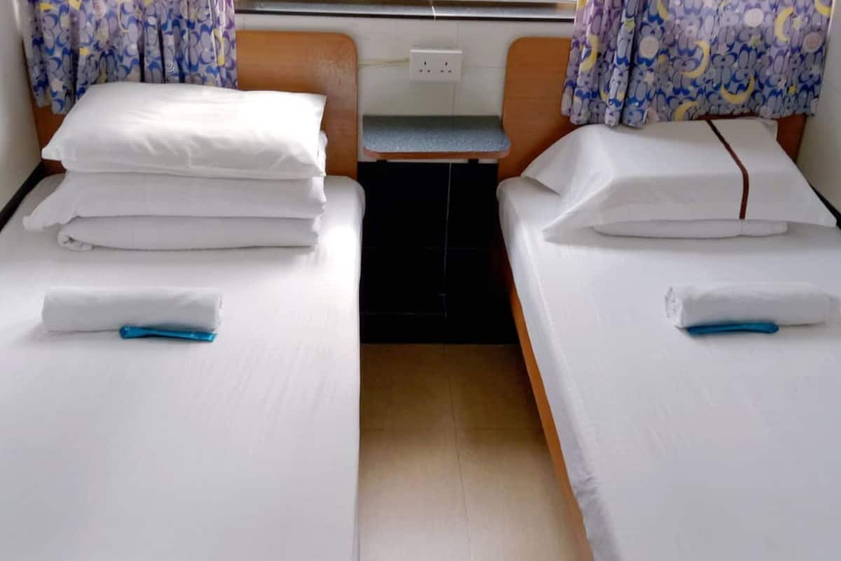 Two single beds with white linens and blue towels, a small table, and a power outlet between them.