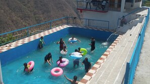 A swimming pool with people and inflatable rings, surrounded by a checkered floor and a view of a mountainous landscape. - The Yamuna Deck Resort and Cafe (Dhanaulti)