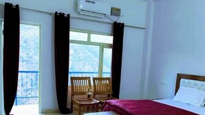 A hotel room with a bed, a ceiling fan, an air conditioning unit, a window with curtains, and a view of the outdoors. - The Yamuna Deck Resort and Cafe (Dhanaulti)