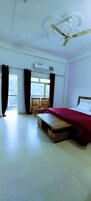 Habitación de hotel con cama, ventilador de techo, aire acondicionado, ventana con cortinas y vistas al exterior.