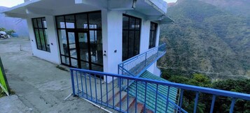 Un edificio pequeño de una sola planta con balcón, rodeado de un paisaje montañoso.