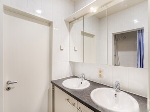 A modern bathroom with two sinks, a mirror, and a shower.