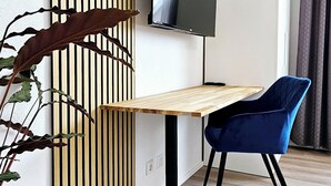A modern room with a wooden slatted partition, a flat-screen TV mounted on the wall, a wooden desk, a blue chair, and a potted plant. - Elodia Luxury Apartment - Wi-Fi, Smart TV, Terrace, Kitchen, Towels (Heidenheim an der Brenz)