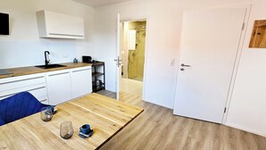 A modern kitchen with white cabinets, a wooden countertop, and a blue chair. There is a door leading to a bathroom with a shower and a towel rack. - Elodia Luxury Apartment - Wi-Fi, Smart TV, Terrace, Kitchen, Towels (Heidenheim an der Brenz)