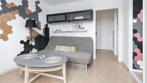 Moderni olohuone, jossa on harmaa sohva, pyöreä pöytä ja kaksi aluslautasta, musta lattiavalaisin sekä seinä, jossa on geometrinen kuvio.