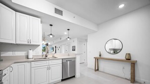 Une cuisine moderne avec des meubles blancs, des appareils en acier inoxydable, des luminaires suspendus et une console en bois.
