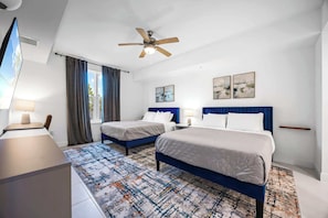 Une chambre d’hôtel avec deux lits, un bureau, une télévision et un ventilateur de plafond.
