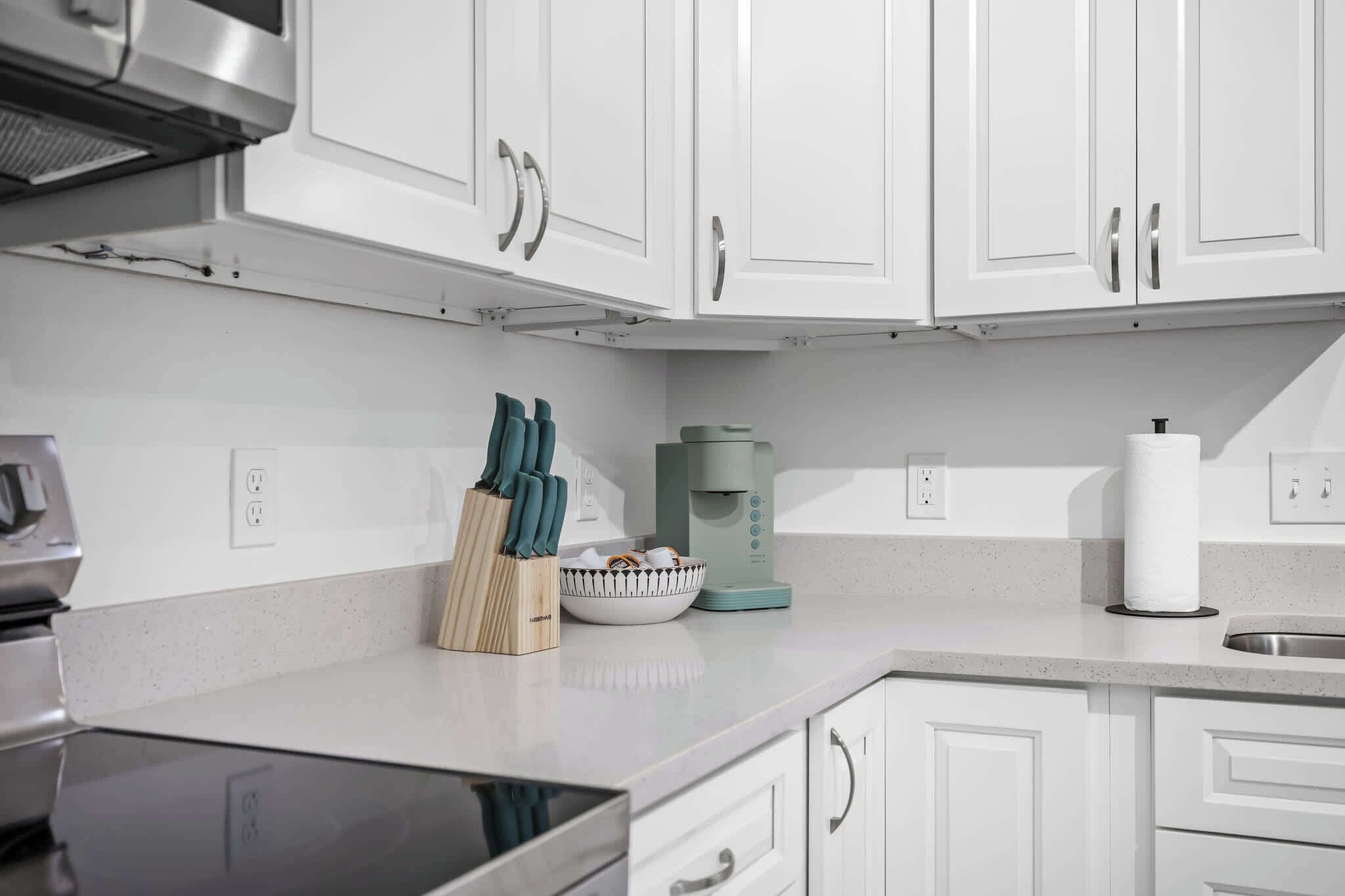 Una cocina moderna con armarios blancos, una cafetera y un cuenco de fruta en la encimera.