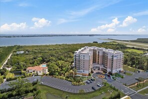 A multi-story hotel with a pool, surrounded by greenery and a body of water.
