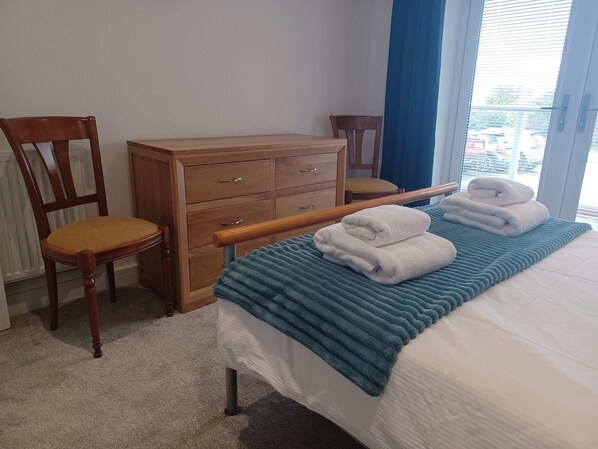 A hotel room with a bed, a wooden dresser, a chair, and a window with a view of parked cars.