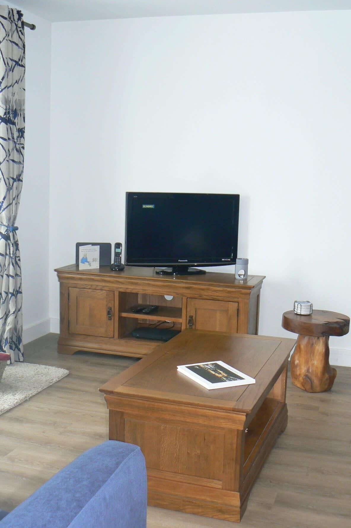 A living room with a wooden cabinet, a flat-screen TV, a coffee table, and a small wooden side table.