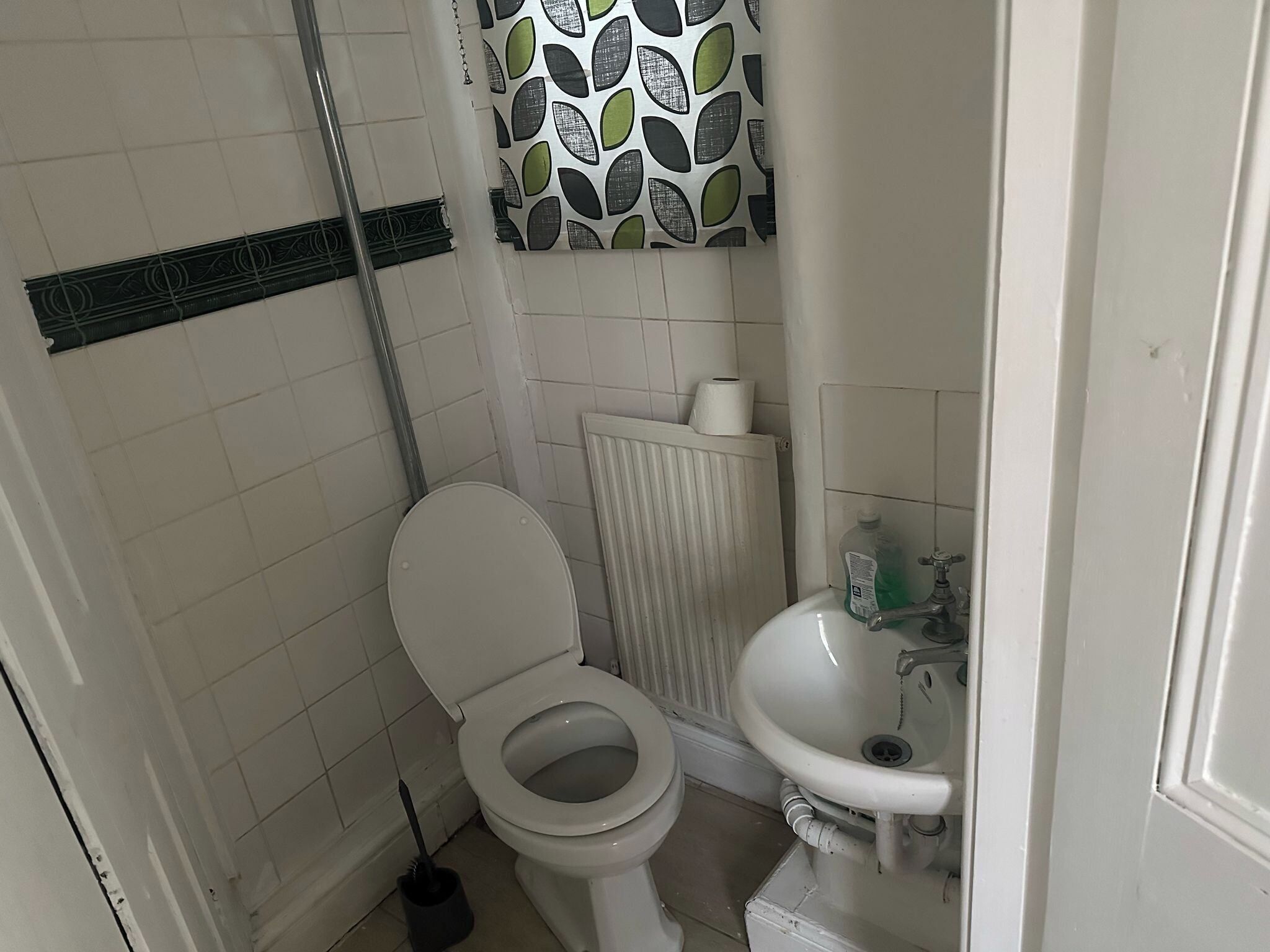 Een kleine badkamer met een toilet, een radiator, een wastafel en een douchegordijn.