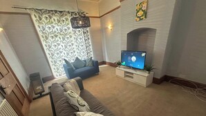 A living room with a sofa, a television on a stand, and a patterned curtain. - House- Parking, Garden & Central Location (Walsall)
