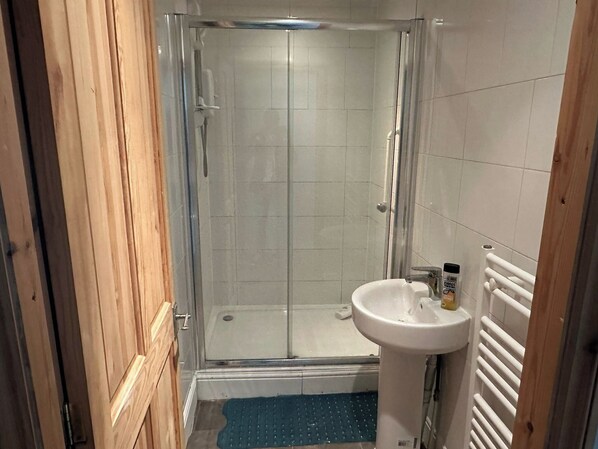 Un baño con cabina de ducha de vidrio, un lavabo blanco y una puerta de madera.