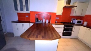 A kitchen with a wooden countertop, white cabinets, and red-tiled backsplash. - House- Parking, Garden & Central Location (Walsall)