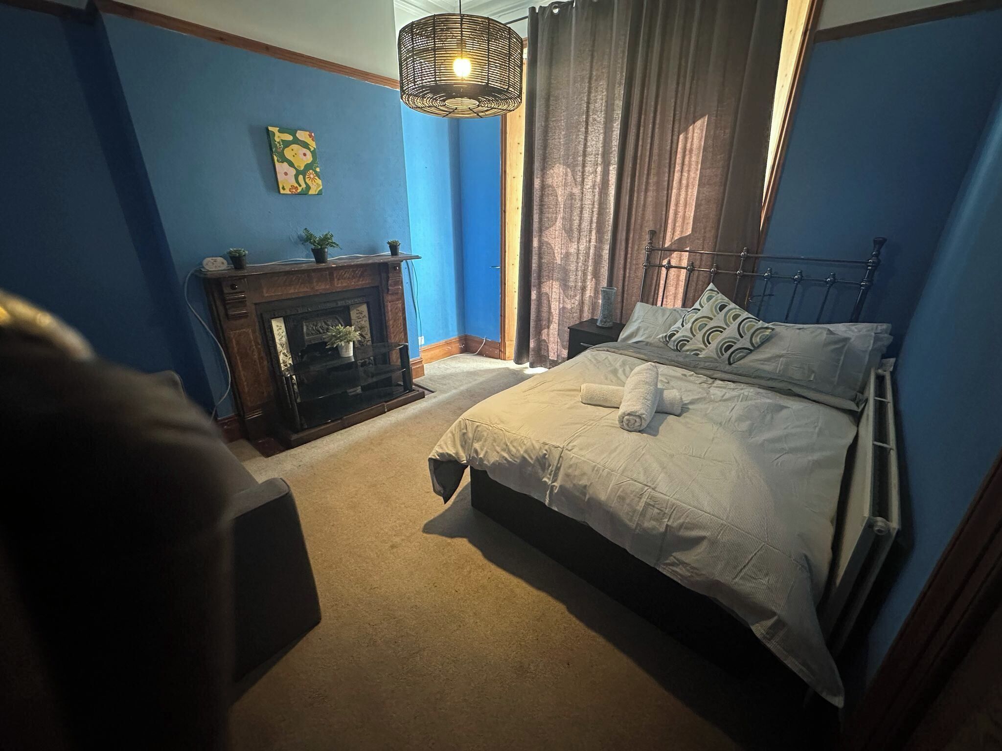 Ein Schlafzimmer mit einem Bett, einem Kamin, einem Nachttisch, einer Lampe und einem Gemälde an der Wand.