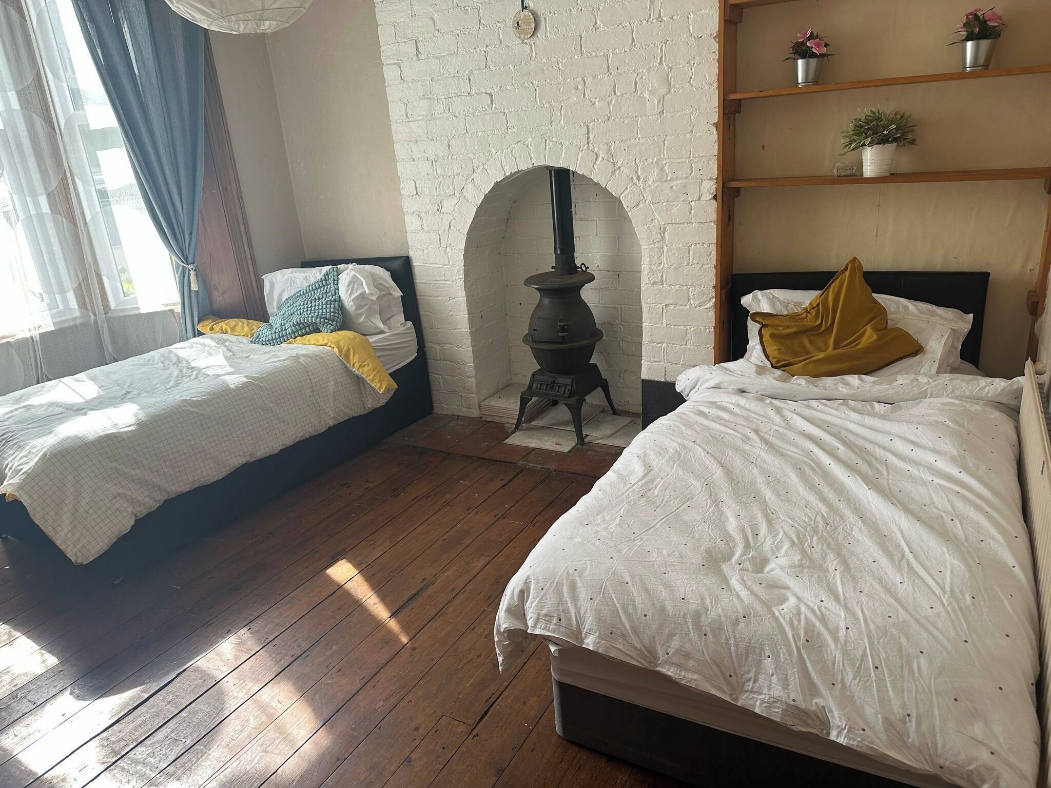 Un dormitorio con dos camas, una pared de ladrillo blanco, piso de madera y una pequeña estufa.