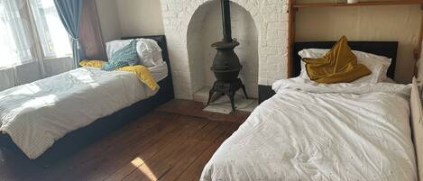 Un dormitorio con dos camas, una pared de ladrillo blanco, piso de madera y una pequeña estufa.