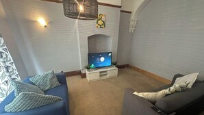 A living room with a blue sofa, a grey sofa, a flat-screen TV, and a decorative wall piece. - House- Parking, Garden & Central Location (Walsall)