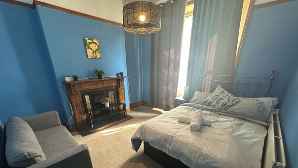 A bedroom with a bed, a chair, a fireplace, and a hanging light fixture. - House- Parking, Garden & Central Location (Walsall)