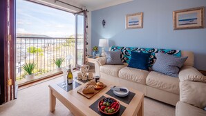 A living room with a sofa, coffee table, and a balcony with a view. - Coastal Escape with Balcony & River Dart Views (Kingswear)