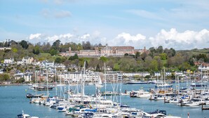 A marina with numerous boats docked, a large building in the background, and a clear sky. - Coastal Escape with Balcony & River Dart Views (Kingswear)