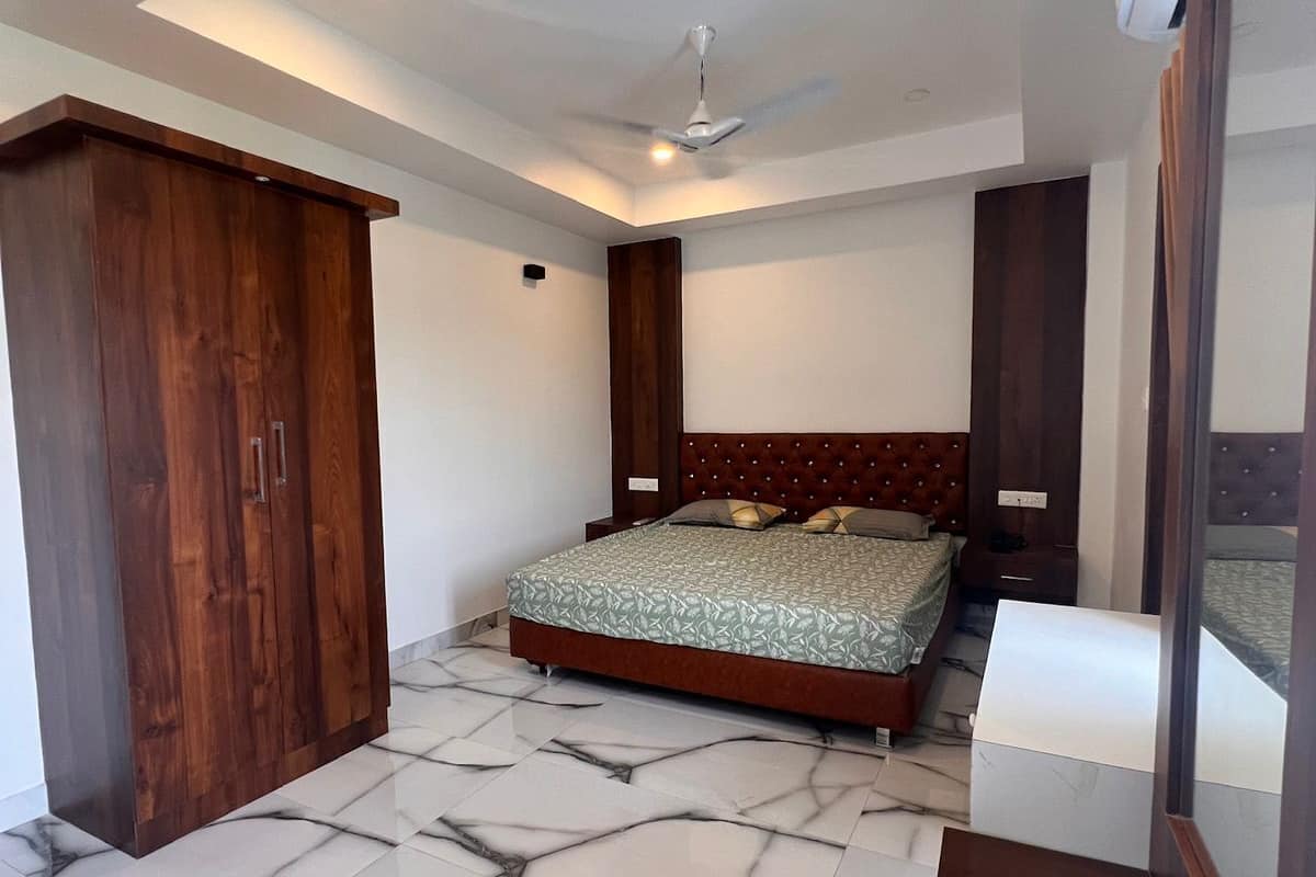 A bedroom with a bed, a wardrobe, a ceiling fan, and a marble floor.