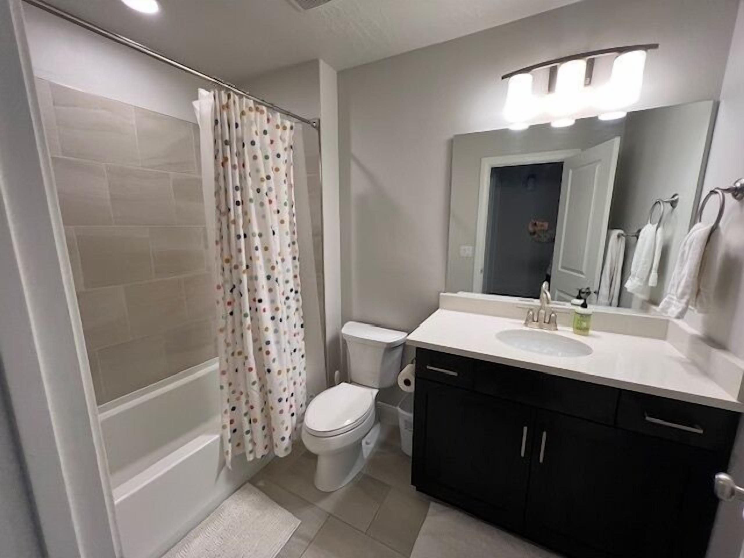 A bathroom with a shower, toilet, sink, and a mirror.