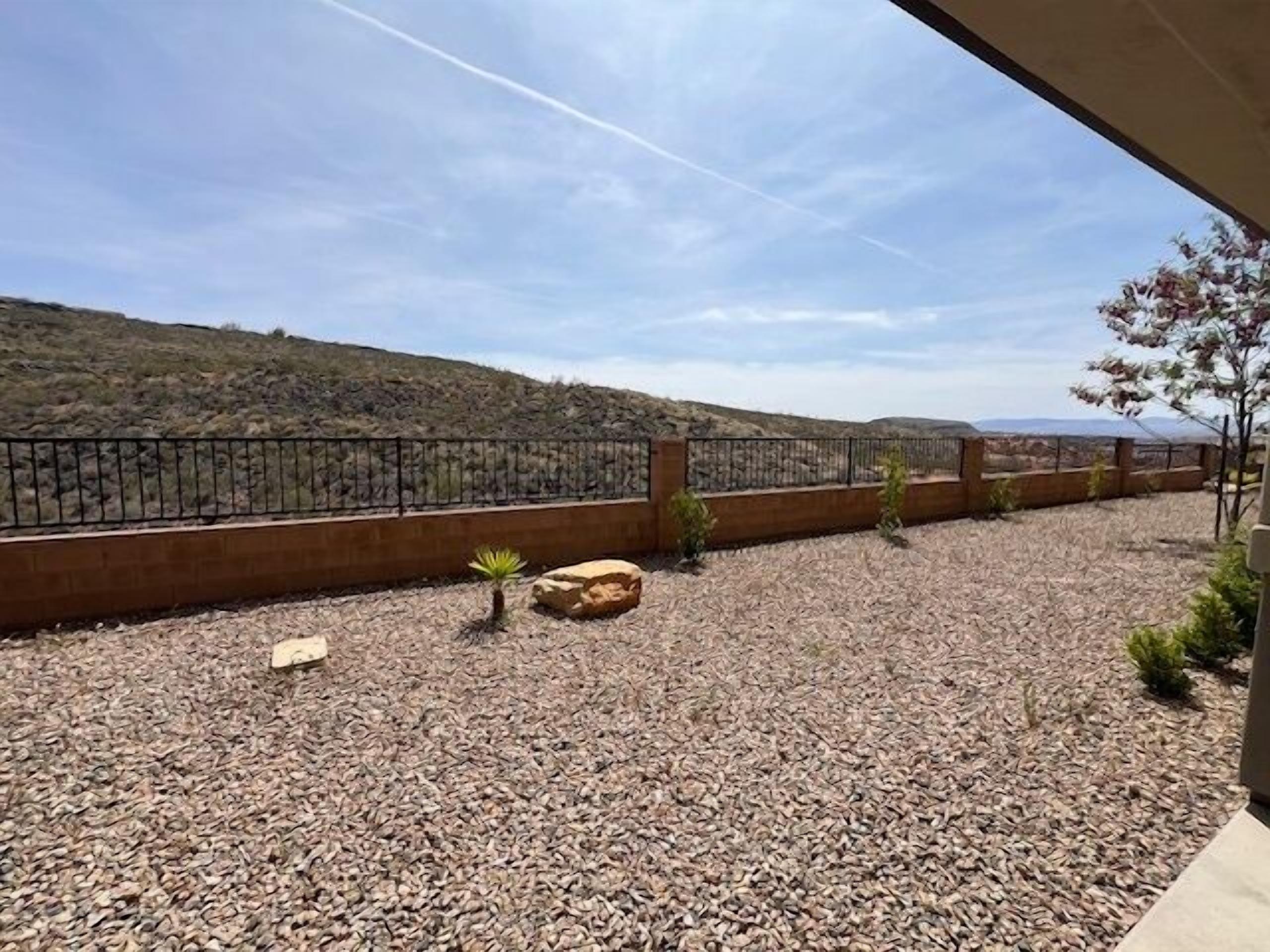 A patio with a view of a hilly landscape, a metal railing, and a few small plants.