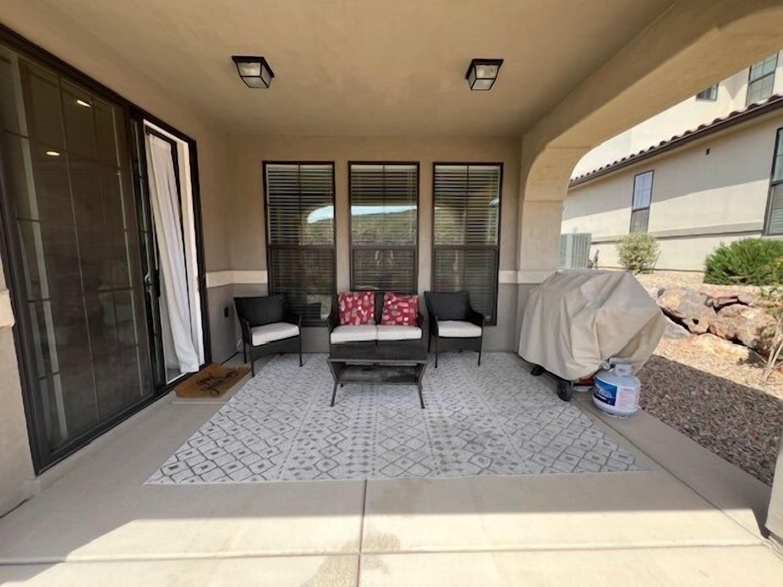 A covered patio with a sofa and chairs, a covered grill, and a patterned floor.