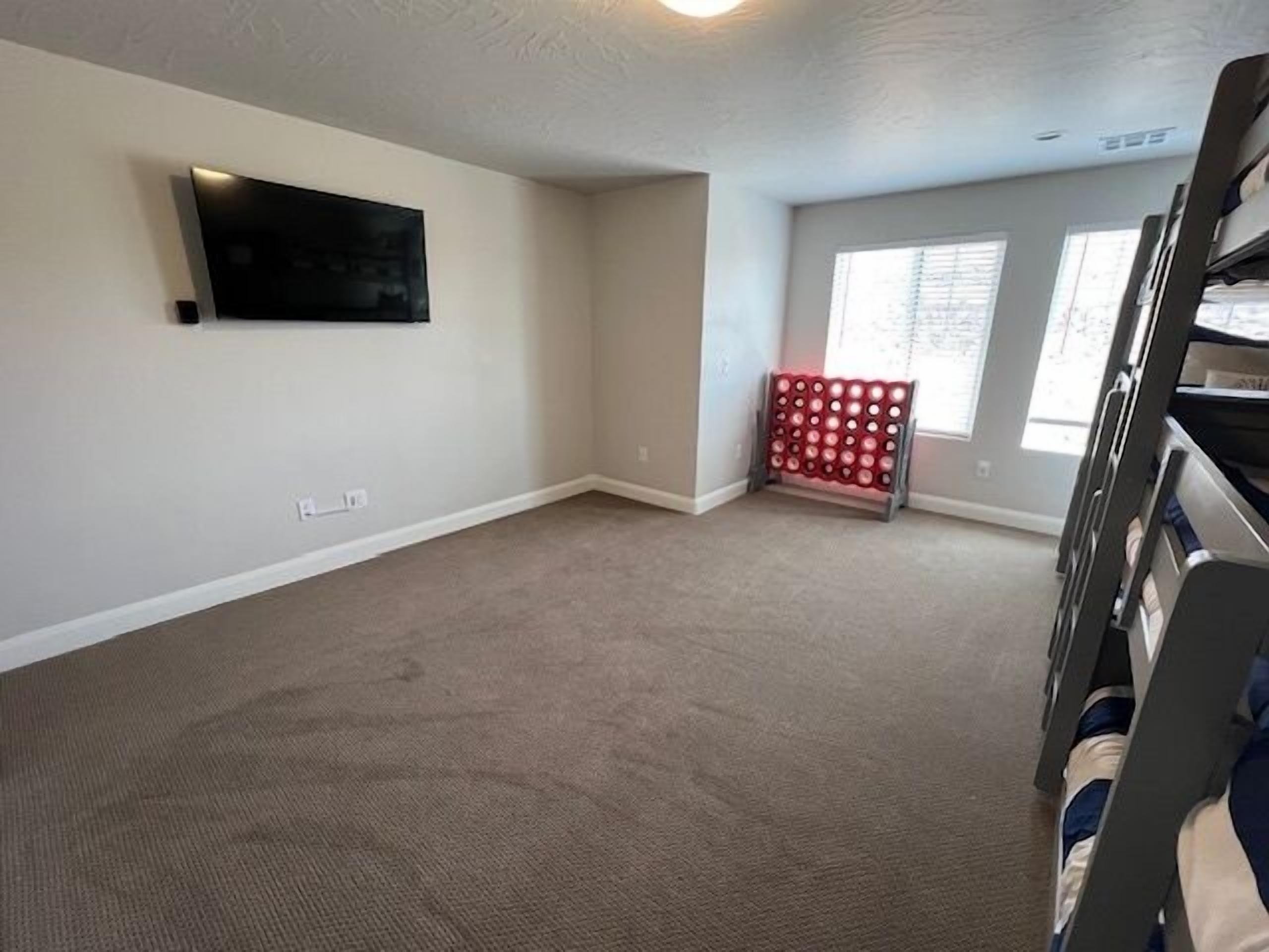 A room with a flat-screen TV mounted on the wall, a red storage unit with circular compartments, and a window with blinds.