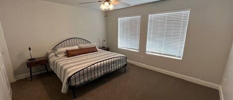 A bedroom with a bed, a ceiling fan, and two windows with blinds.