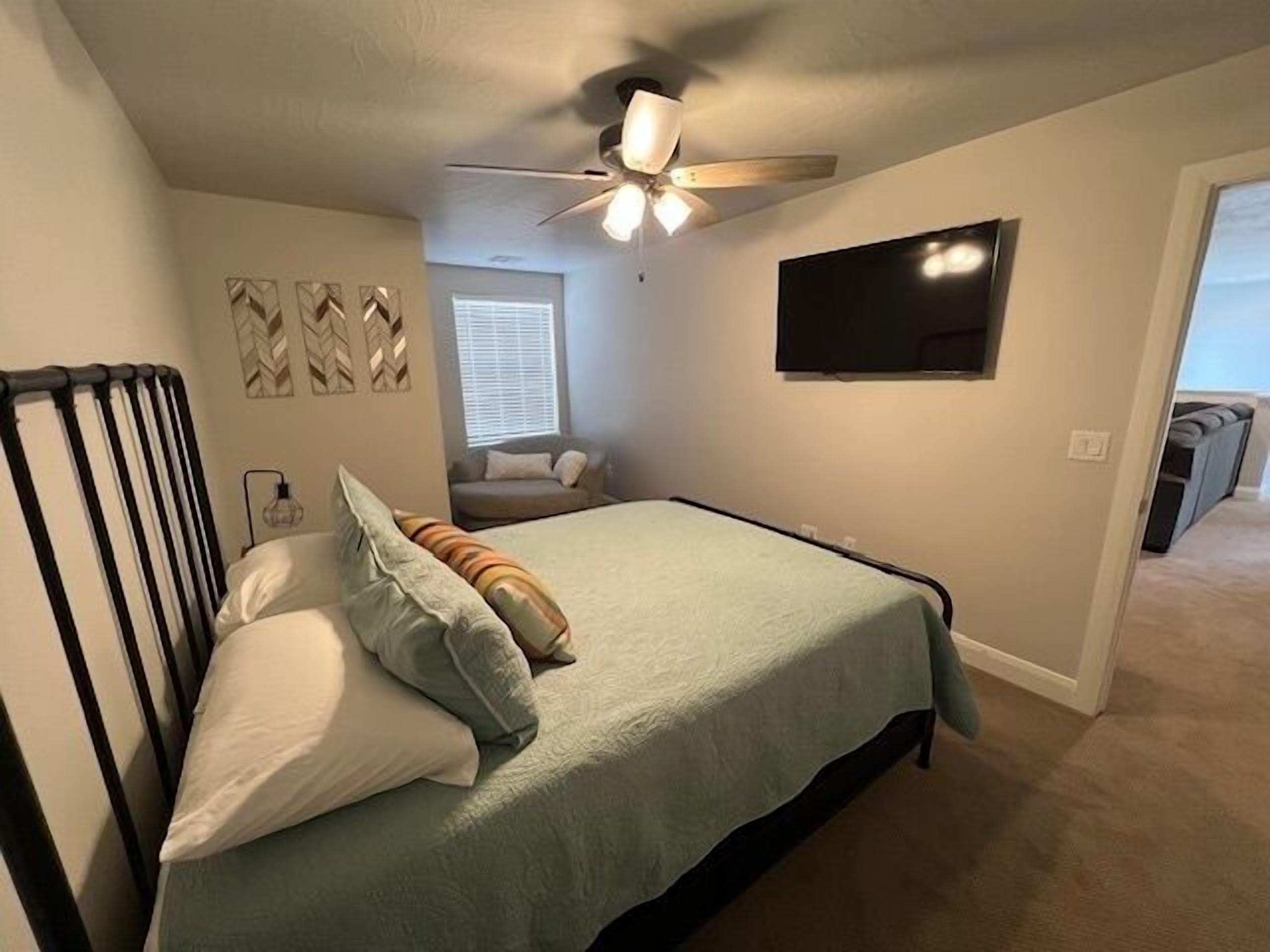 A bedroom with a bed, a ceiling fan, a TV, and a window.