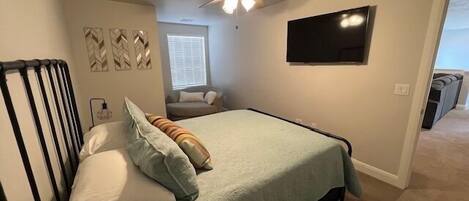 A bedroom with a bed, a ceiling fan, a TV, and a window.